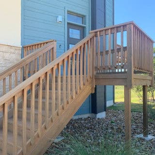 Wooden staircase leading to a blue building with a door, surrounded by grass and rocks.